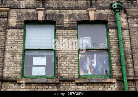 Lagerfenster über einem Geschäft, Vorräte in Fenstern des Geschäfts über dem Gelände, Lagerraum, Kleidung, die im Fenster des Lagerraums hängt, Schiebefenster. Stockfoto