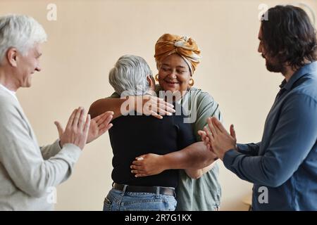 Porträt von einer vielfältigen Gruppe älterer Menschen, die applaudieren und sich umarmen, während sie Erfolge in der Selbsthilfegruppe feiern Stockfoto