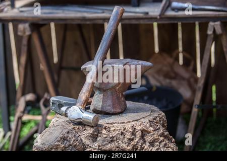 Amboss, Hammer und Pfeffer über dem Korkeichenstumpf. Schmied-Werkzeuge aus einem alten römischen Militärlager. Stockfoto