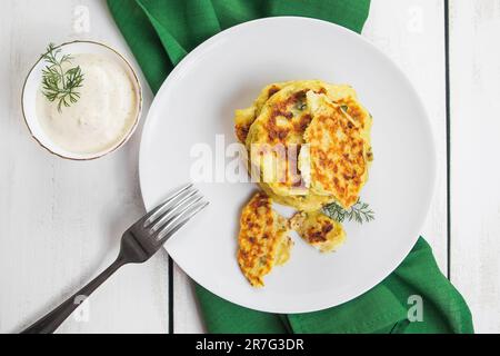 Teller mit Gemüsezucchini-Frittern auf weißem Holztisch. Gesunde vegane Ernährung, Draufsicht. Auf grüner Serviette. Stockfoto