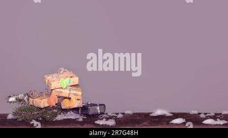 Geschenkschachteln, Papierherzen und Tannenzweig auf einem Holzbrett. Winterweihnachten, Neujahr mit lila Akzent. Stockfoto
