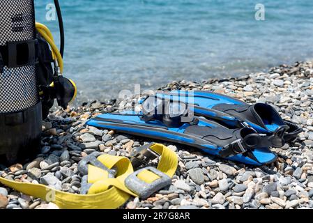 Tauchausrüstung, einschließlich Sauerstofftank, Flossen, Schutzbrille, Regler und Gewichte am Ufer eines felsigen Strandes. Wassersport. Einführung in das Sporttauchen Stockfoto