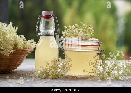 Flaschen hausgemachter alter Blütensirup mit frischen Blüten auf einem Tisch im Freien Stockfoto