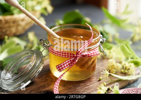 Ein Glas Honig mit frischen Lindenblumen und Blättern im Hintergrund Stockfoto