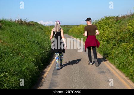 Rückansicht von zwei Freunden, die im Sommer an einem sonnigen Tag im Frühjahr 2023 auf einer Landstraße spazieren. Pembrokeshire Wales UK KATHY DEWITT Stockfoto
