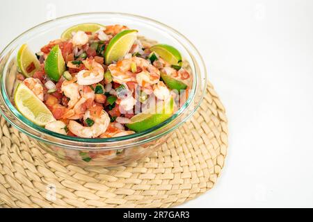 Frischer Garnelensalat mit Limettenscheiben in einer Glasschüssel auf einer Bambusmatte, isoliert auf Weiß Stockfoto