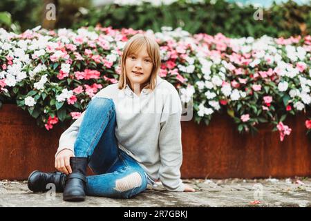 Außenporträt eines lustigen kleinen Mädchens mit grauem Sweatshirt, Jeans und schwarzen Stiefeln Stockfoto