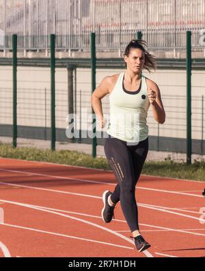 Junge, starke, entschlossene weiße Sportlerin in der Startposition auf Bahn 4 auf der Laufbahn Stockfoto