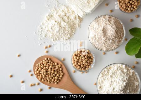 Ganzer und raffinierter Sojabohnenmehl und Sojabohnen in Glasschüsseln und Holzlöffel auf weißem Tisch. Draufsicht. Stockfoto