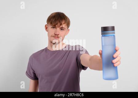 Mann mit transparenter Kunststoffflasche und Getränk auf hellgrauem Hintergrund Stockfoto