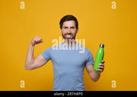 Mann mit grüner Wärmflasche mit Arm auf orangefarbenem Hintergrund Stockfoto