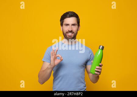 Mann mit grüner Wärmflasche zeigt eine OK-Geste auf orangefarbenem Hintergrund. Platz für Text Stockfoto