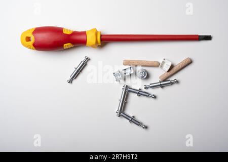 Ein Schlitz- oder Schlitzschraubendreher und ein Stapel von Teilen eines neuen Möbels, verschiedene Montagemöbelbeschläge. Stockfoto