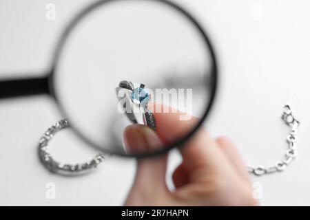 Juwelier, der den Topaz-Ring mit einer Lupe am weißen Tisch untersucht, Nahaufnahme Stockfoto