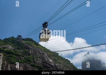 Klettern mit der Zuckerhut-Seilbahn auf den Gipfel des Urca-Hügels mit dem Zuckerhut, der von Wolken im Hintergrund unter dem wolkigen Himmel am Sommernachmittag umgeben ist. Stockfoto