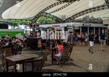 Touristen, die vorbeilaufen und andere nehmen sich Zeit im überdachten Food Court von Urca Hill im Stadtteil Urca, in der Nähe einiger Geschäfte an einem sonnigen Sommertag. Stockfoto