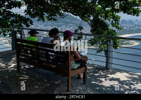 Touristen, die sich an einem sonnigen Sommernachmittagstag auf einer Holzbank unter Baumschatten am Geländer der Aussichtsplattform des Urca Hill aufhalten. Stockfoto