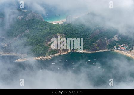 Teilweise aus der Vogelperspektive auf den Babilonia-Hügel und das blaue Wasser des Atlantischen Ozeans durchblickten dicke Wolken vom Gipfel des Zuckerhuts aus. Stockfoto