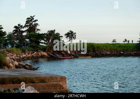 Große Felsen und einige Fischerboote in der Nähe Bäume am Santos Dumont Felsenpier (Pier de Pedra) im Centro District unter blauem Himmel am späten Sommer-Nachmittag. Stockfoto