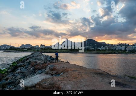 Blick auf den Sonnenuntergang am Santos Dumont Rock Pier (Pier de Pedra), in der Nähe des Flughafens Santos Dumont am Gloria-Viertel, an der Küste unter bewölktem Himmel. Stockfoto