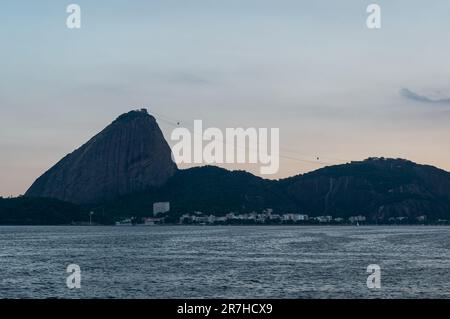 Der Zuckerhut und der Urca-Hügel sind Naturdenkmäler mit sichtbaren Seilbahnen zwischen ihnen in den Gewässern der Guanabara-Bucht am Sommernachmittag. Stockfoto