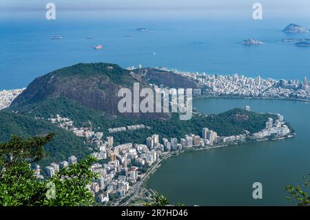 Teilweise aus der Vogelperspektive auf die Viertel Lagoa und Ipanema mit dem Morro dos Cabritos-Hügel dazwischen, wie vom Berg Corcovado unter sonnigen, trüben Sommerhimmel gesehen. Stockfoto