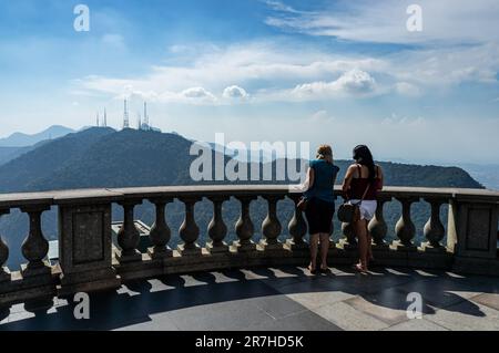 Zwei weibliche Touristen genießen den Blick auf den Westen auf dem Gipfel des Corcovado Berges, nahe Christusstatue der Erlöser unter dem wolkigen Himmel am Sommernachmittag. Stockfoto