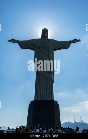 Volle Vorderansicht der Christusstatue mit Sonne dahinter auf dem Gipfel des Corcovado, umgeben von Touristen an sonnigen Sommertagen. Stockfoto