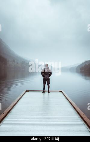 Ein Mann steht allein am Rande eines Piers und blickt auf das Wasser und den fernen Horizont Stockfoto