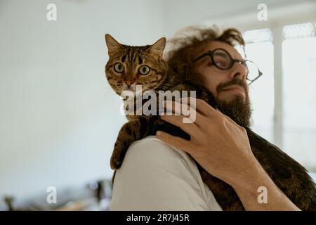 Der gutaussehende junge Tierliebhaber umarmt die Katze während der Ruhezeit zu Hause Stockfoto