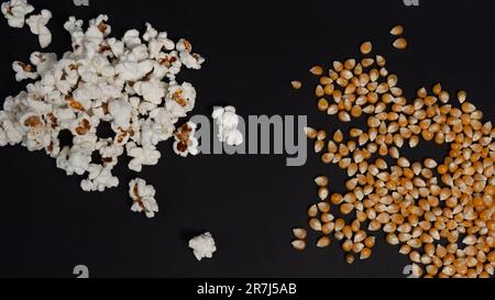 Zwei Stapel Popcorn, ein Stapel Fertigpopcorn, ein weiterer mit Maiskernen, Popcorn auf schwarzem Hintergrund, Popcorn zum Fernsehen. Stockfoto