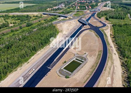 Leipzig, Deutschland. 12. Juni 2023. Die erste Asphaltschicht wurde bereits auf die zukünftige Fahrbahn der A72 am Zwenkau-Kreuz bei Großdeuben aufgetragen. Die Kluft zwischen den A72 und den A38 Jahren sollte bis Mitte Juli geschlossen sein. Bis 2026 sollen die meisten Neubauarbeiten abgeschlossen sein, und der Verkehr von Vogtland nach Leipzig wird auf zwei Fahrspuren fahren können. Der Bau der Lückenschließung ist komplex, da die Strecke über die Ablageflächen eines ehemaligen Tagebaues führt. (Luftfoto mit Drohne) Kredit: Jan Woitas/dpa/Alamy Live News Stockfoto