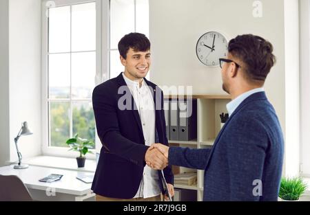 Lächelnder Geschäftsführer, der seinem Partner die Hand schüttelt, nachdem er sich in einem modernen Büro getroffen hat. Stockfoto