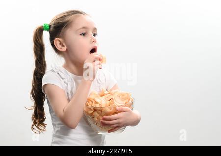 Ein Mädchen nimmt Chips Snacks mit Schmalz aus einer Schüssel und isst sie, Porträt auf weißem Hintergrund und Kopierraum, ungesunde und ungesunde Nahrung. Stockfoto