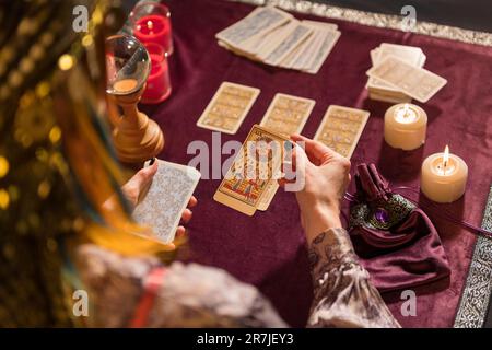 Eine anonyme Wahrsagerin, die eine Tarotkarte pflückt, während sie mit brennenden Kerzen und Kristall am Tisch sitzt Stockfoto