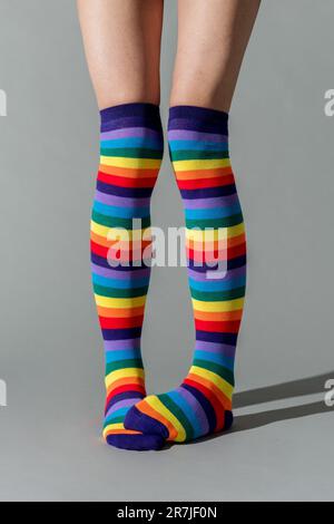 Zugeschnittene Beine einer nicht wiedererkennbaren Frau in gestreiften, bunten Socken, die im Studio vor grauem Hintergrund stehen und Schatten auf dem Boden haben Stockfoto