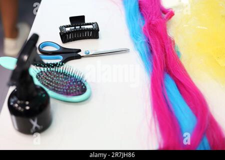 Eine Komposition mit farbigem Haar, Kamm, Schere und einem Platz für Text auf farbigem Hintergrund. Friseurdienstleistungen. Stockfoto