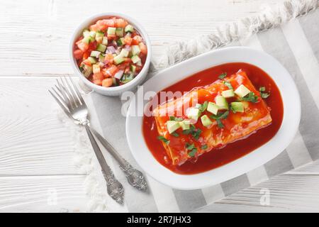 Leckere, nasse Burritos mit Rindfleisch, Reis und gekühlten Bohnen, verpackt in einer Tortilla, erstickt mit roter Sauce, auf dem Teller auf dem Holztisch. Stockfoto