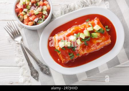 Nasse Burritos haben ein Hackfleisch und gekühlte Bohnenfüllung, verpackt in eine große Tortilla, erstickt mit roter Sauce und geschmolzenem Käse, auf dem Teller o Stockfoto