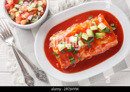 Ein nasses Burrito-Rezept mit Mehltortillas gefüllt mit Hackfleisch, gekühlten Bohnen und Chiles, geschlossen auf dem Teller auf dem Holztisch. Horizontal t Stockfoto