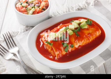 Nasse Burritos haben ein Hackfleisch und gekühlte Bohnenfüllung, verpackt in eine große Tortilla, erstickt mit roter Sauce und geschmolzenem Käse, auf dem Teller o Stockfoto