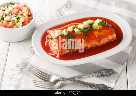 Ein nasses Burrito-Rezept mit Mehltortillas gefüllt mit Hackfleisch, gekühlten Bohnen und Chiles, geschlossen auf dem Teller auf dem Holztisch. Horizontal Stockfoto