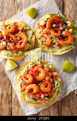 Tostadas mit saftigen Garnelen, cremiger Avocado Guacamole und scharfer Salsa-Nahaufnahme auf dem Holztisch. Vertikale Draufsicht von oben Stockfoto