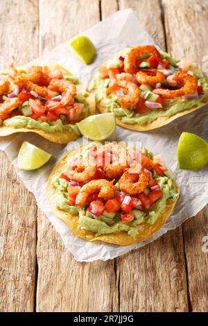 Köstliche Tostada mit Garnelen, frischem Gemüse und Guacamole aus nächster Nähe auf einem Holztisch. Vertikal Stockfoto