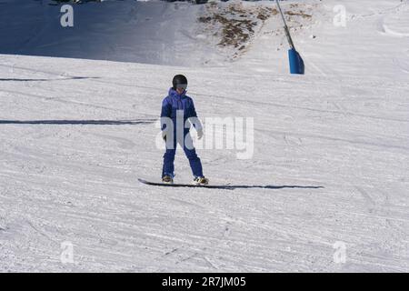 Ein Junge mit Snowboard mit Schutzhelm und Skimaske hat Spaß auf einer Schneeskipiste in den italienischen Dolomiten. Stockfoto