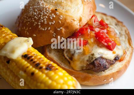 Ein frisch gegrillter Hamburger mit hausgemachtem Relish befindet sich auf einem Teller neben einem Rumpf gegrilltem Bio-Mais mit Butter in Seattle, Washington. Stockfoto