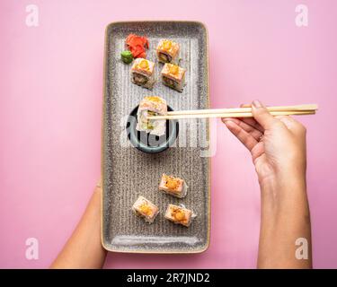 Ein Blick von oben auf eine elegante Platte mit Sushi-Rollen vor einem leuchtend rosa Hintergrund Stockfoto
