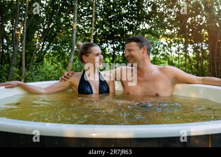 Romantisches Paar, das sich im Wannen-Whirlpool im Freien mit Holzfeuer im Wald erholt Stockfoto
