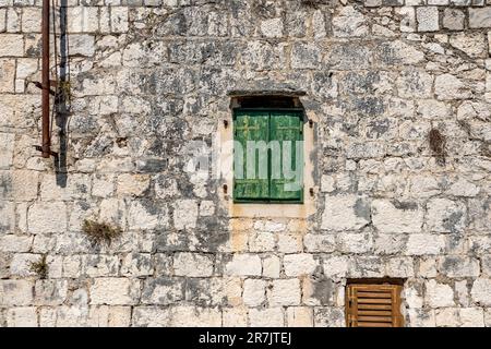 Typisches altes Haus mit verwitterten, geschlossenen grünen Holzläden und Steinmauer, Rogoznica Dorf, Dalmatien, Kroatien Stockfoto