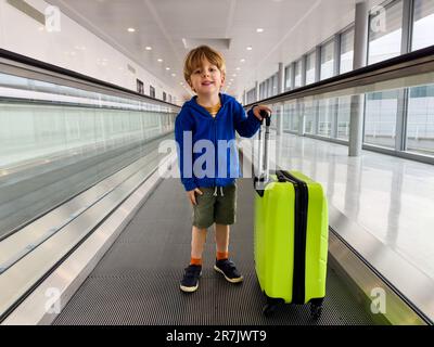 Das Kind steht auf einem bewegenden Gang am Flughafen mit Koffer Stockfoto